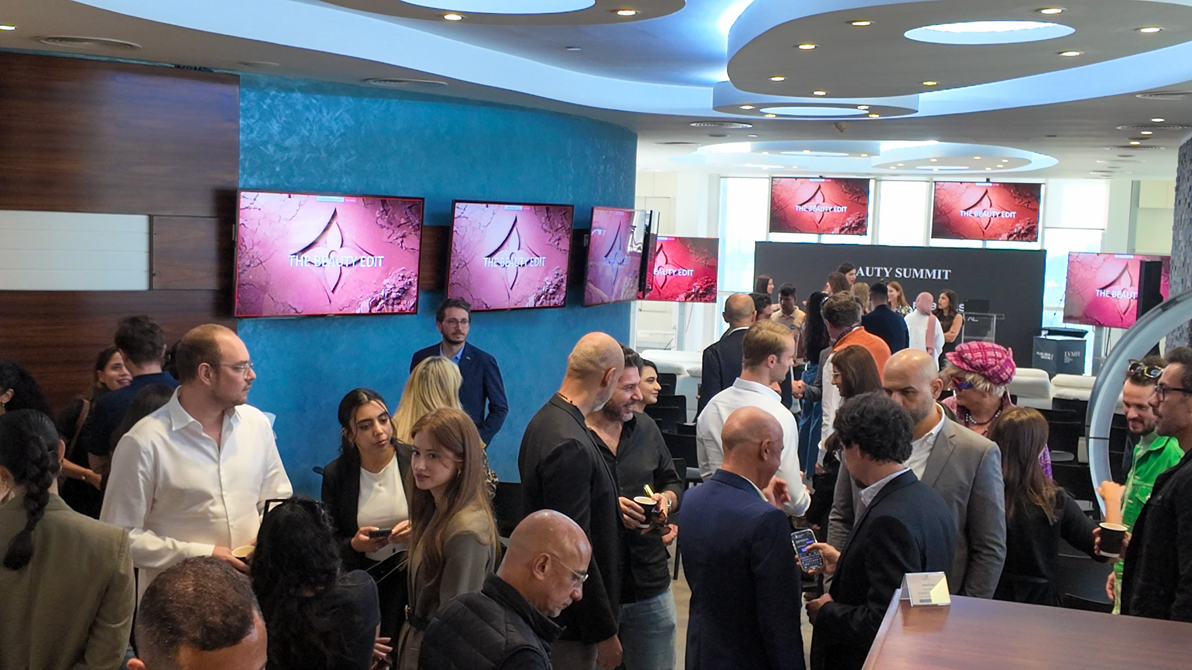 Attendees networking at a Beauty Summit event with screens displaying 'The Beauty Edit' branding.